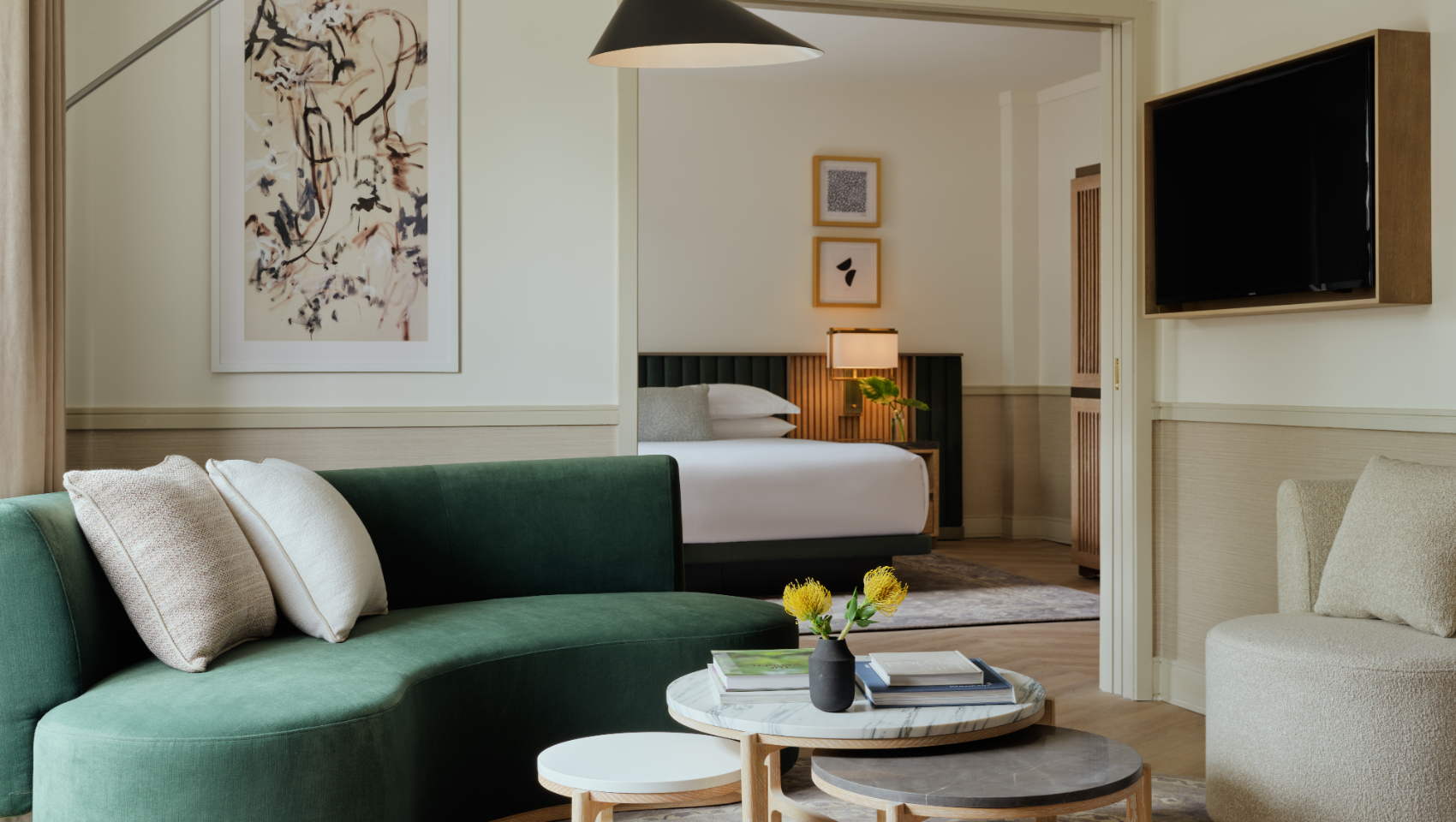 Elegant living room with a green curved sofa, contemporary nesting tables, and a bright bedroom beyond