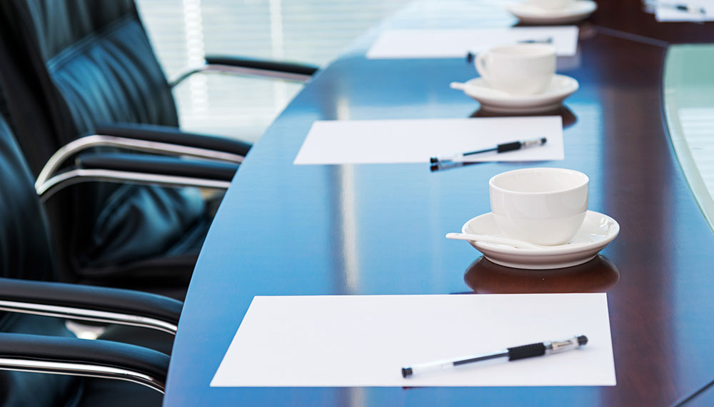 Meeting room table with black chairs, paper and pen and coffee cup